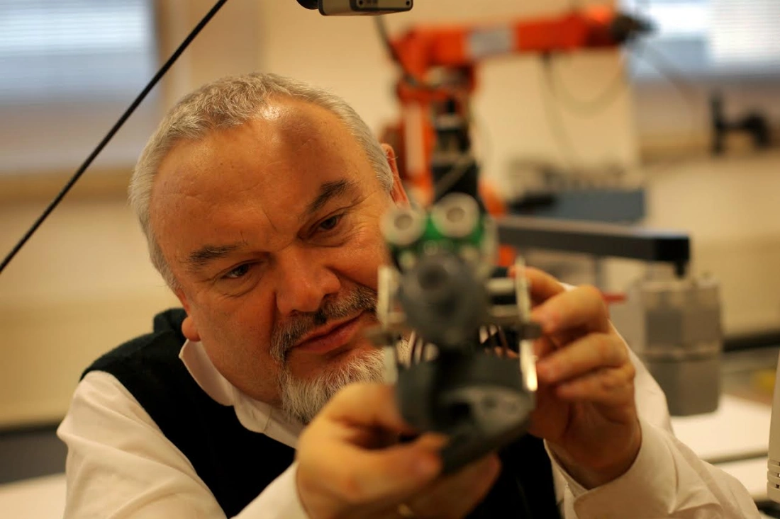 Mężczyzna w białej koszuli i czarnym kamizelce bada mały model z detali technicznych w warsztacie.