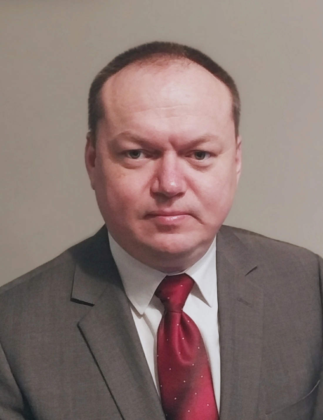 Mężczyzna w garniturze z krawatem, stojący na neutralnym tle.