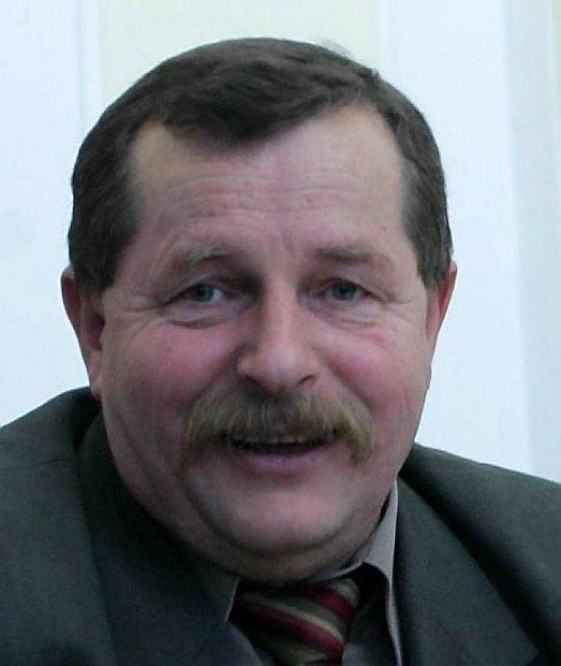 Mężczyzna z mustachami uśmiecha się w formalnym ubraniu.