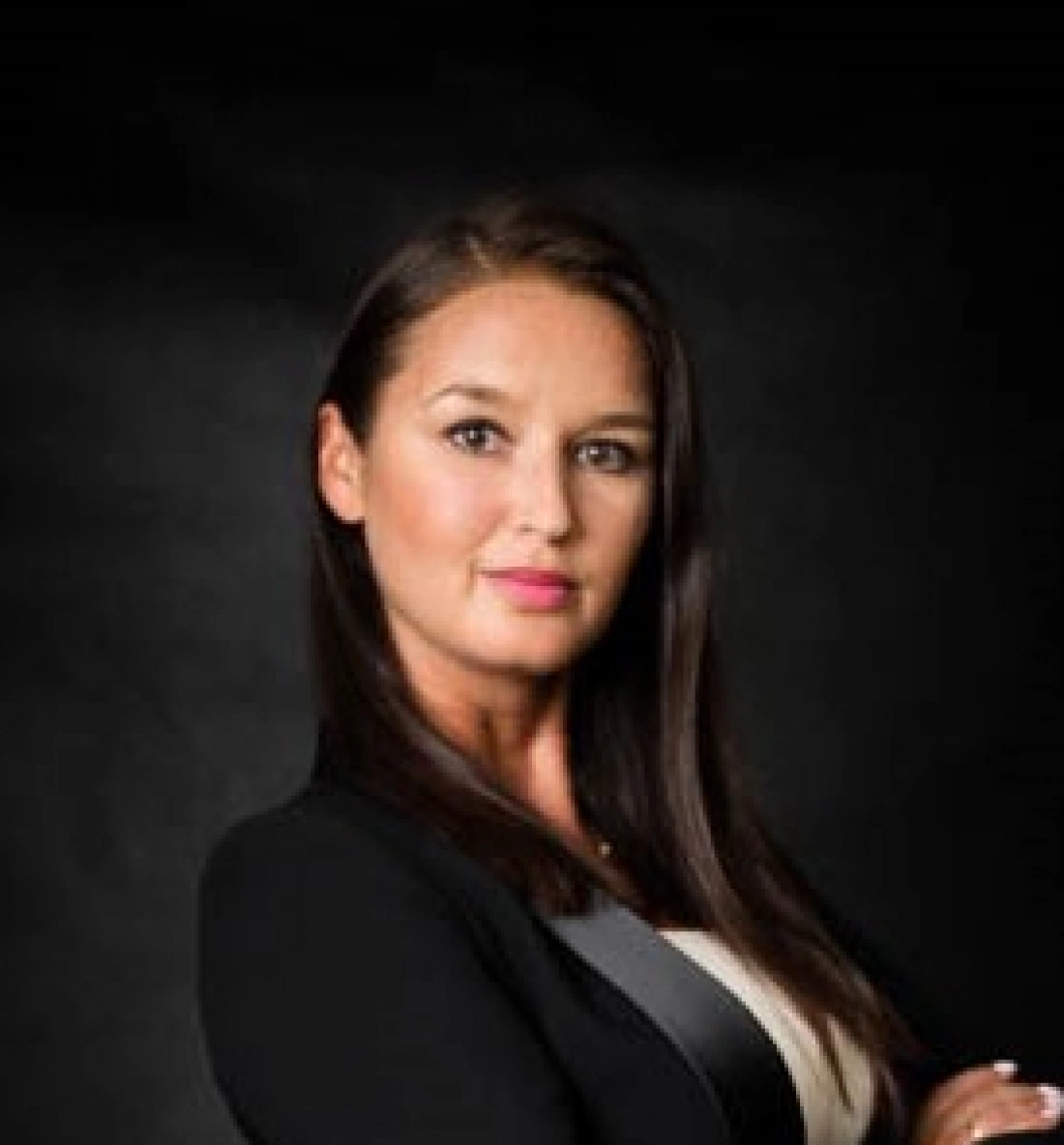 Kobieta w eleganckim ubraniu, z długimi włosami, pozująca na ciemnym tle.