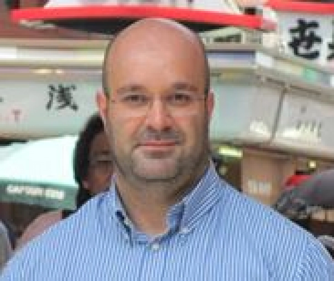 Mężczyzna w okularach na tle ulicy z napisami.