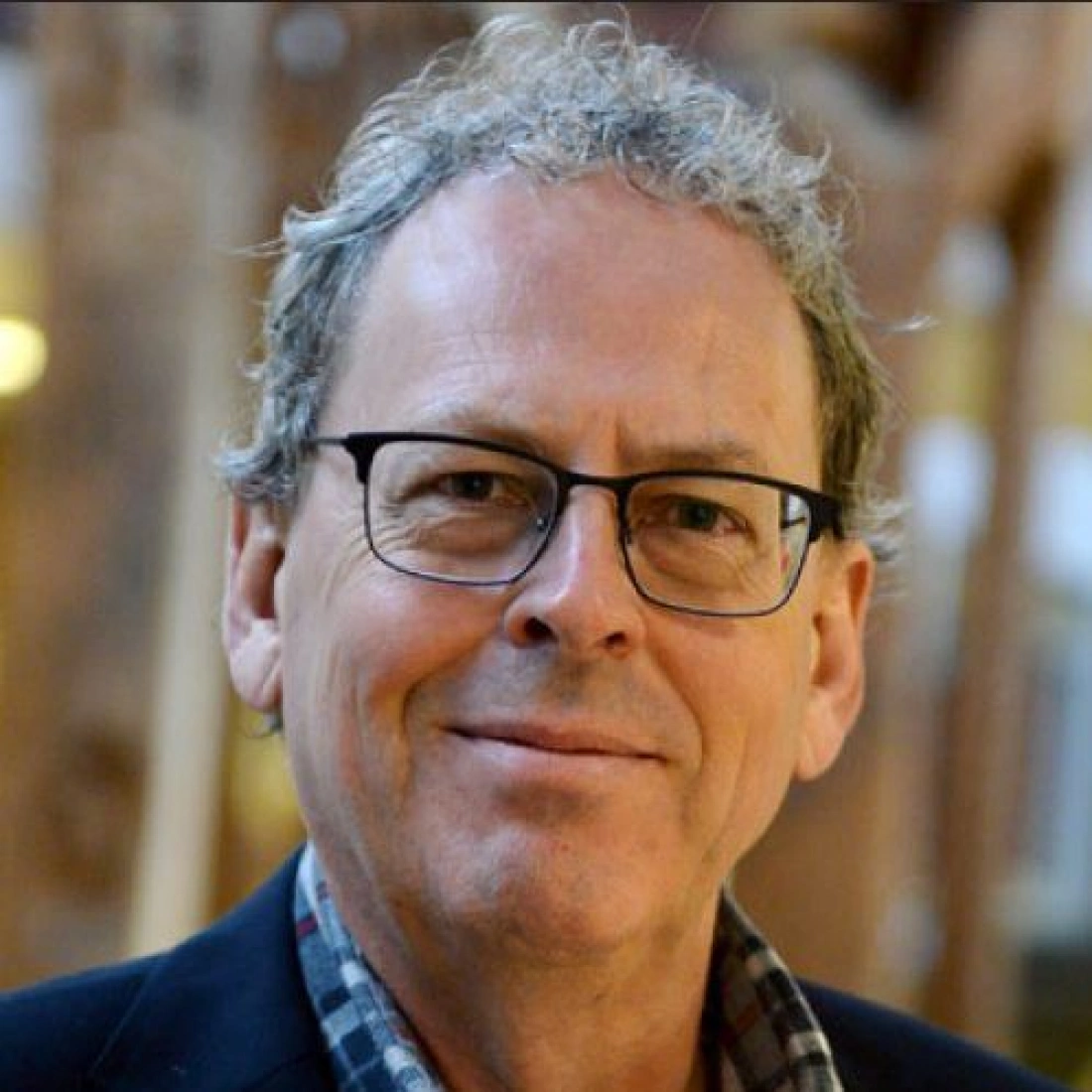 Mężczyzna w okularach z uśmiechem na tle drewnianej struktury.