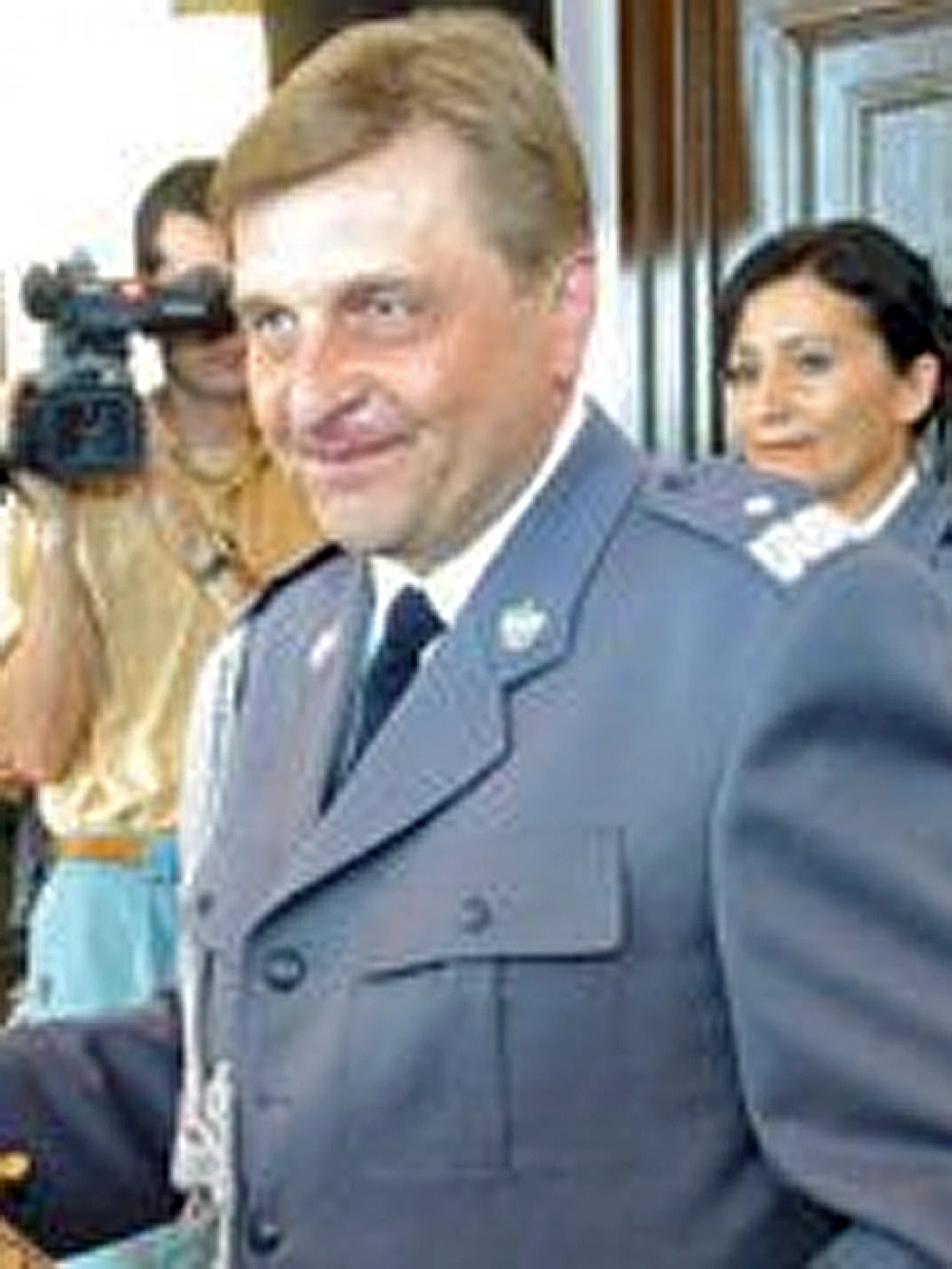 Mężczyzna w mundurze z uśmiechem, stojący w towarzystwie innych osób.