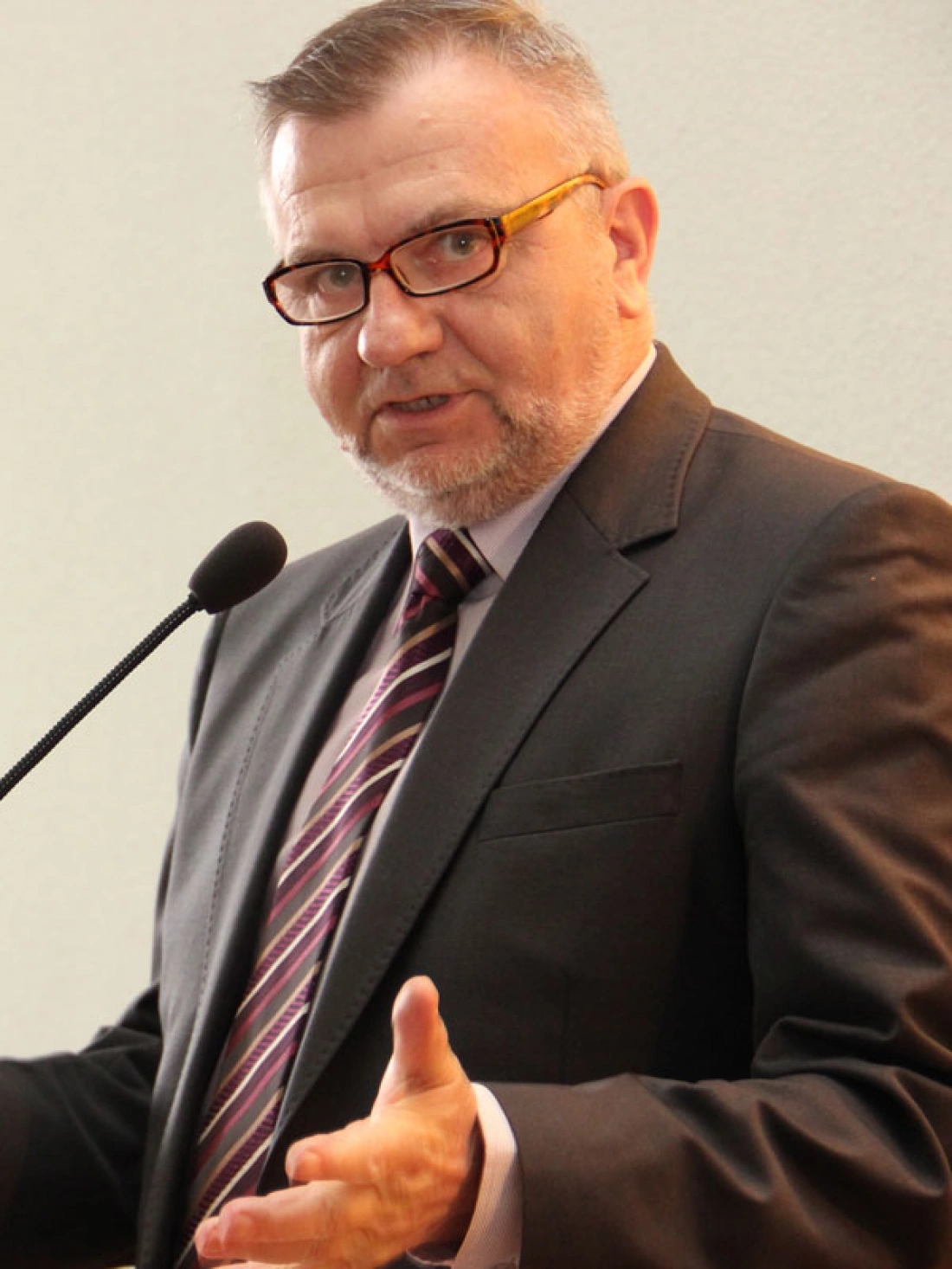Mężczyzna w garniturze wygłasza przemówienie, trzymając rękę w gestykulacji.