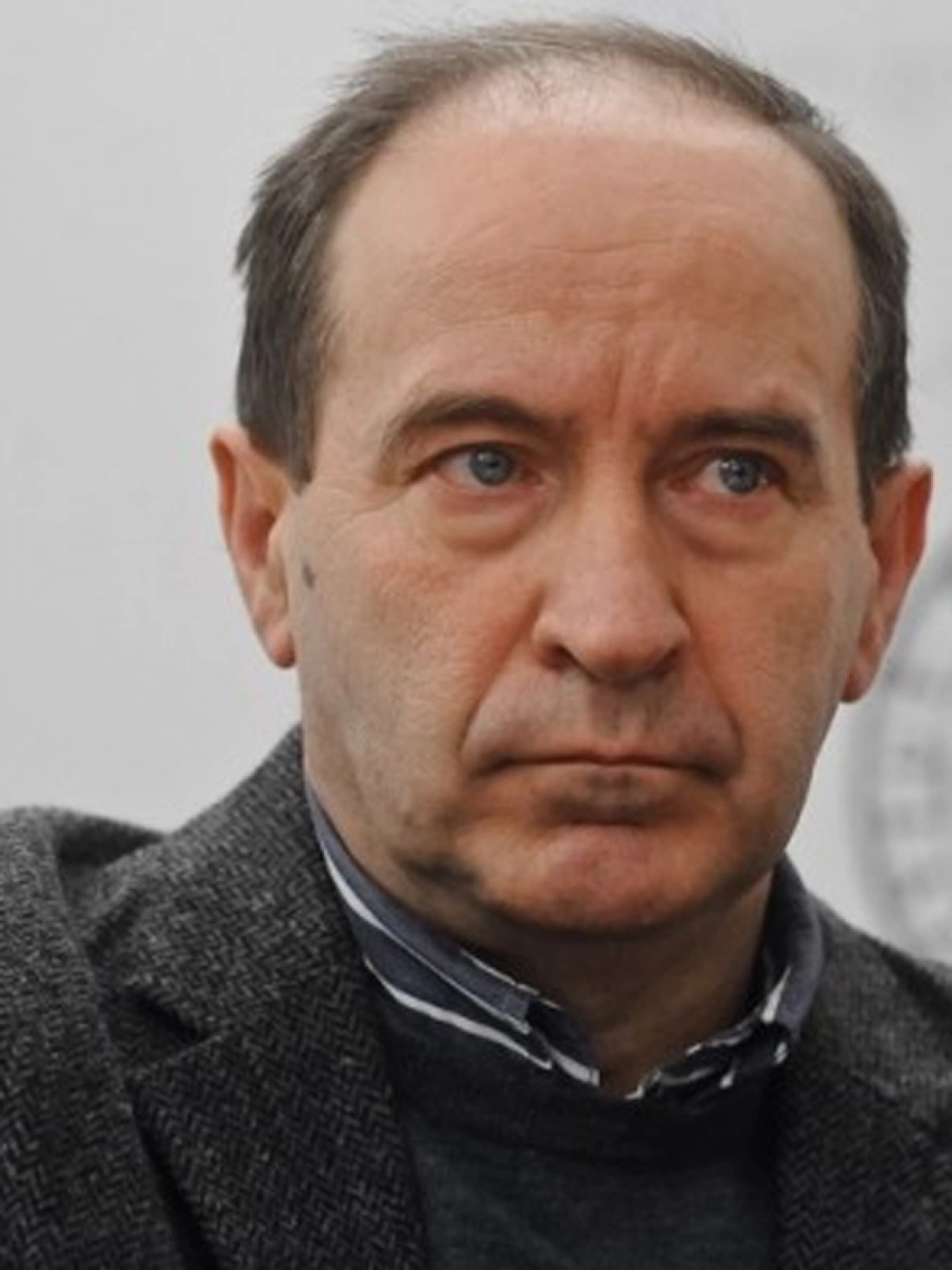 Mężczyzna z krótkimi, brązowymi włosami, w szarej marynarce, z poważnym wyrazem twarzy.