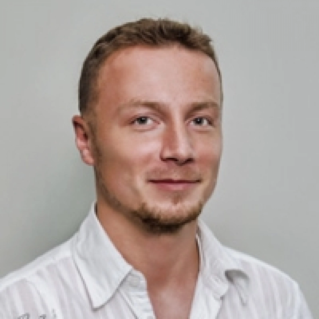 Mężczyzna w jasnej koszuli, uśmiechający się.