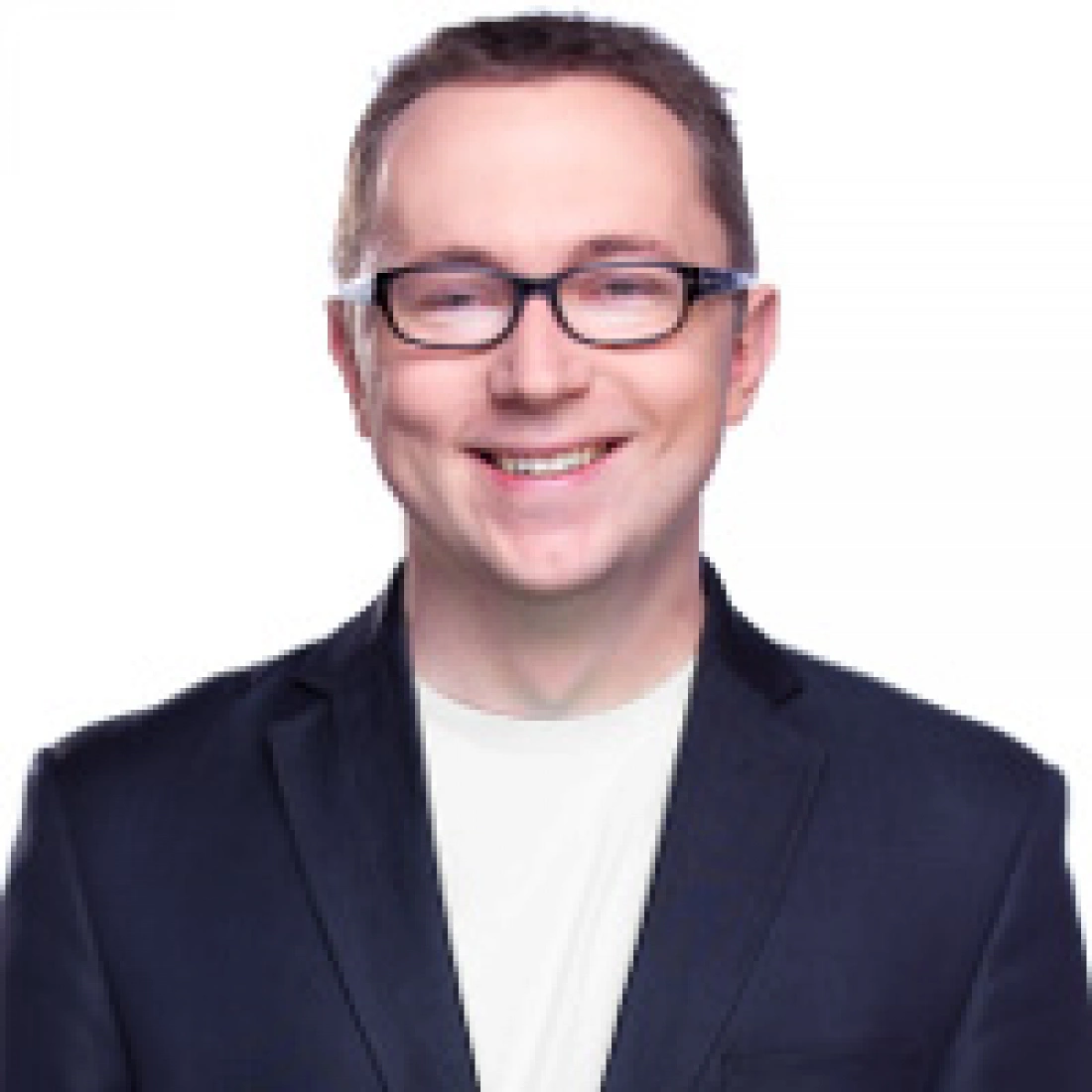 Osoba w okularach, uśmiechająca się, ubrana w ciemną marynarkę i jasną koszulę.