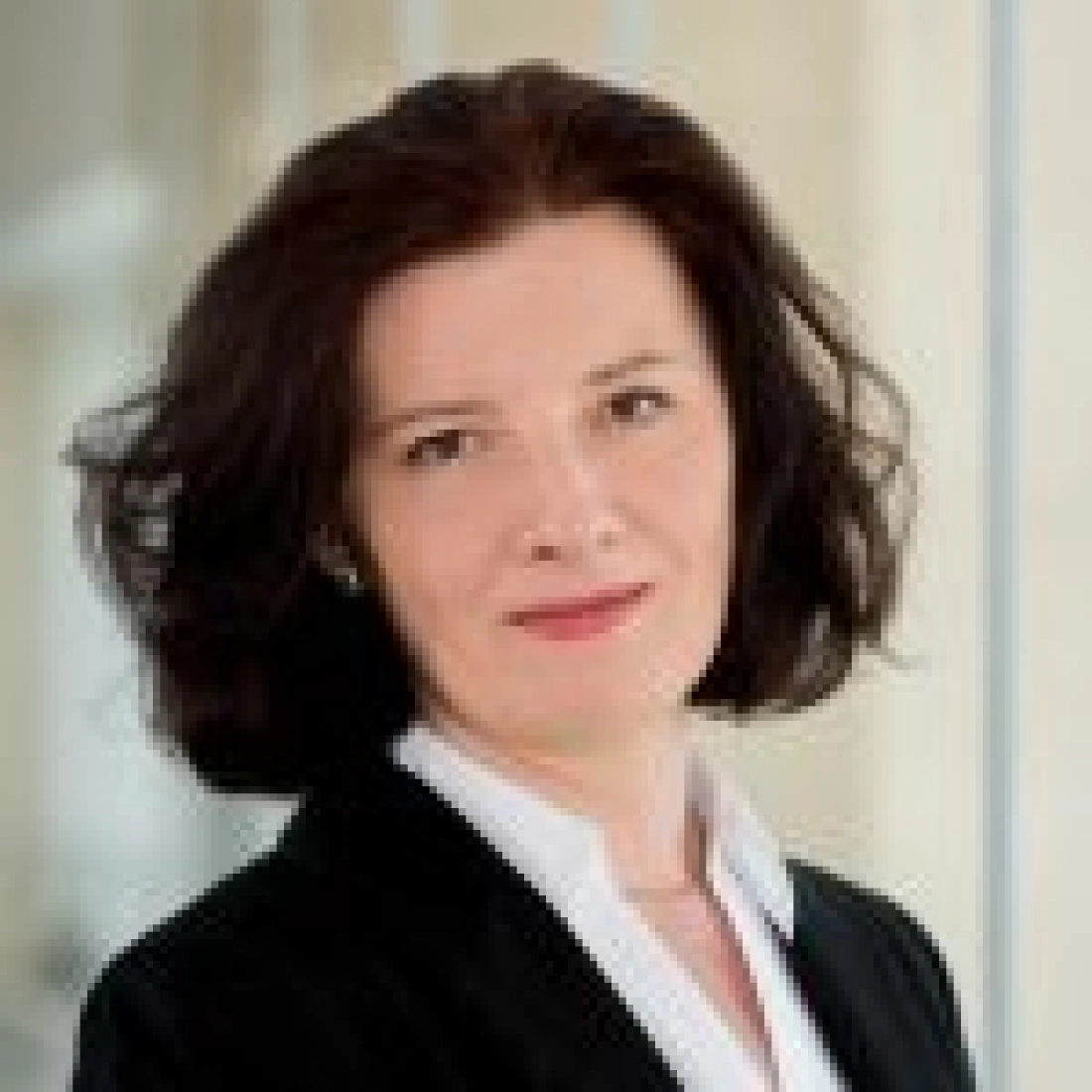 Kobieta w formalnym ubraniu z uśmiechem, stojąca w biurowym otoczeniu.