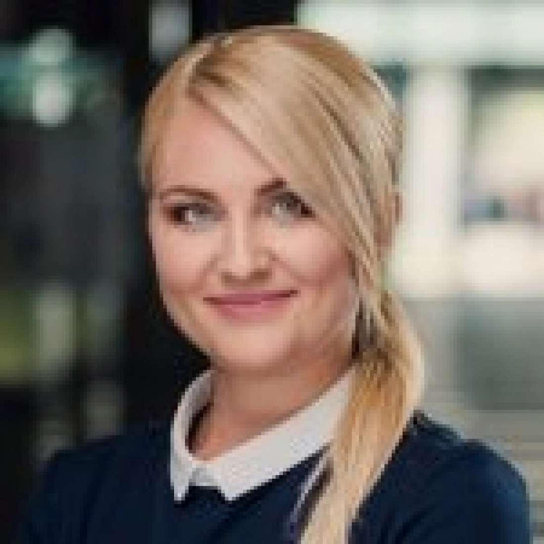 Kobieta z długimi blond włosami, uśmiechająca się, w eleganckim stroju.