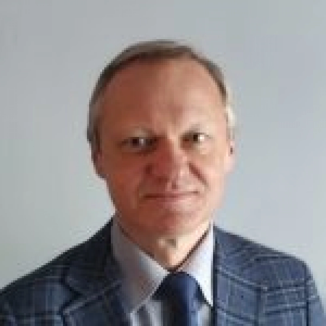 Mężczyzna w garniturze z uśmiechem, stojący na neutralnym tle.