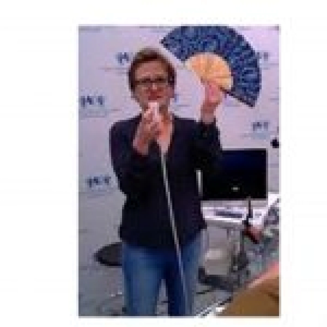 Kobieta trzyma wachlarz i mikrofon, stojąc w biurze.