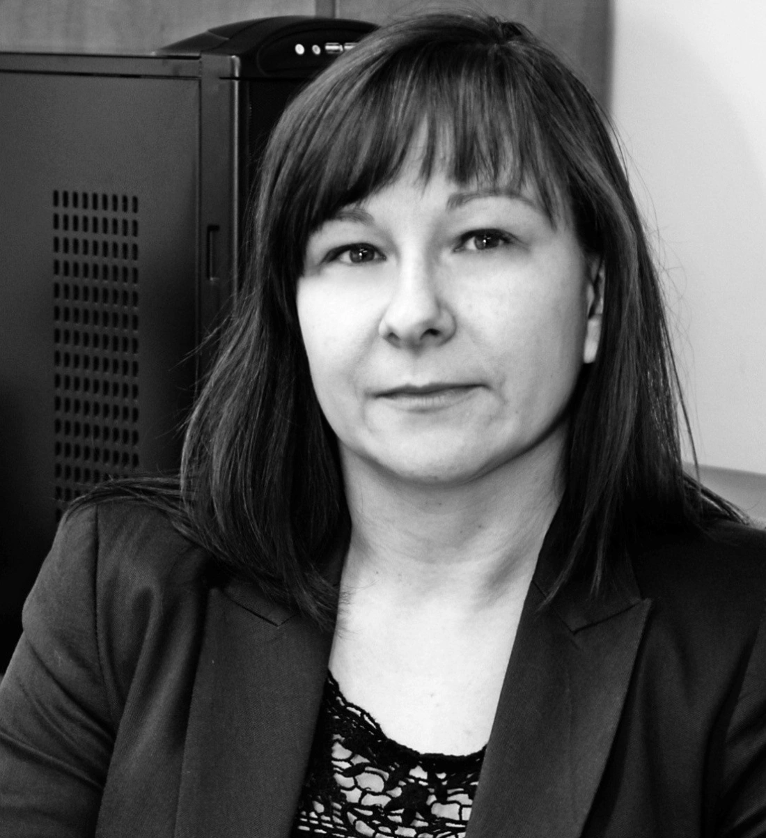 Kobieta w marynarce, siedząca przy biurku w czarno-białym ujęciu.