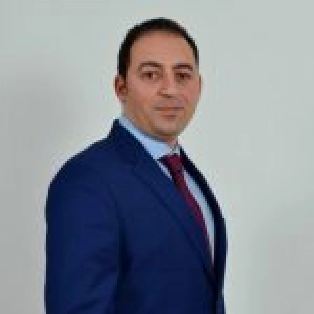 Mężczyzna w garniturze z krawatem, stojący na neutralnym tle.