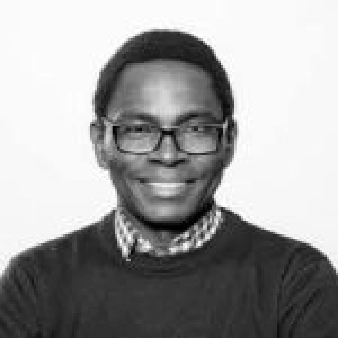 Mężczyzna w okularach, uśmiechający się na tle jasnej ściany.