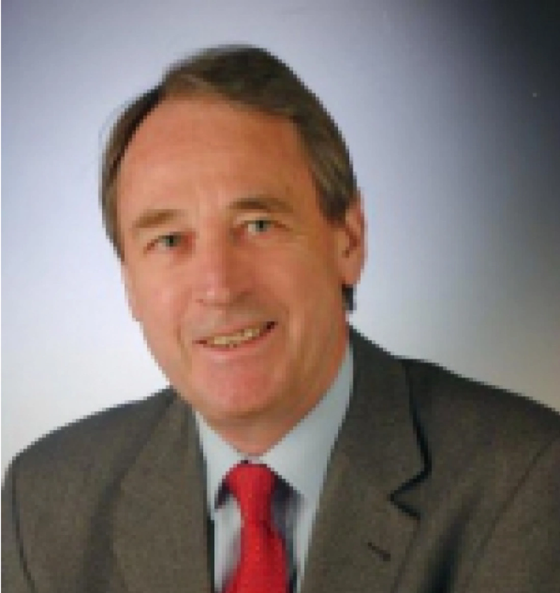 Mężczyzna w garniturze z uśmiechem na tle jednolitego tła.