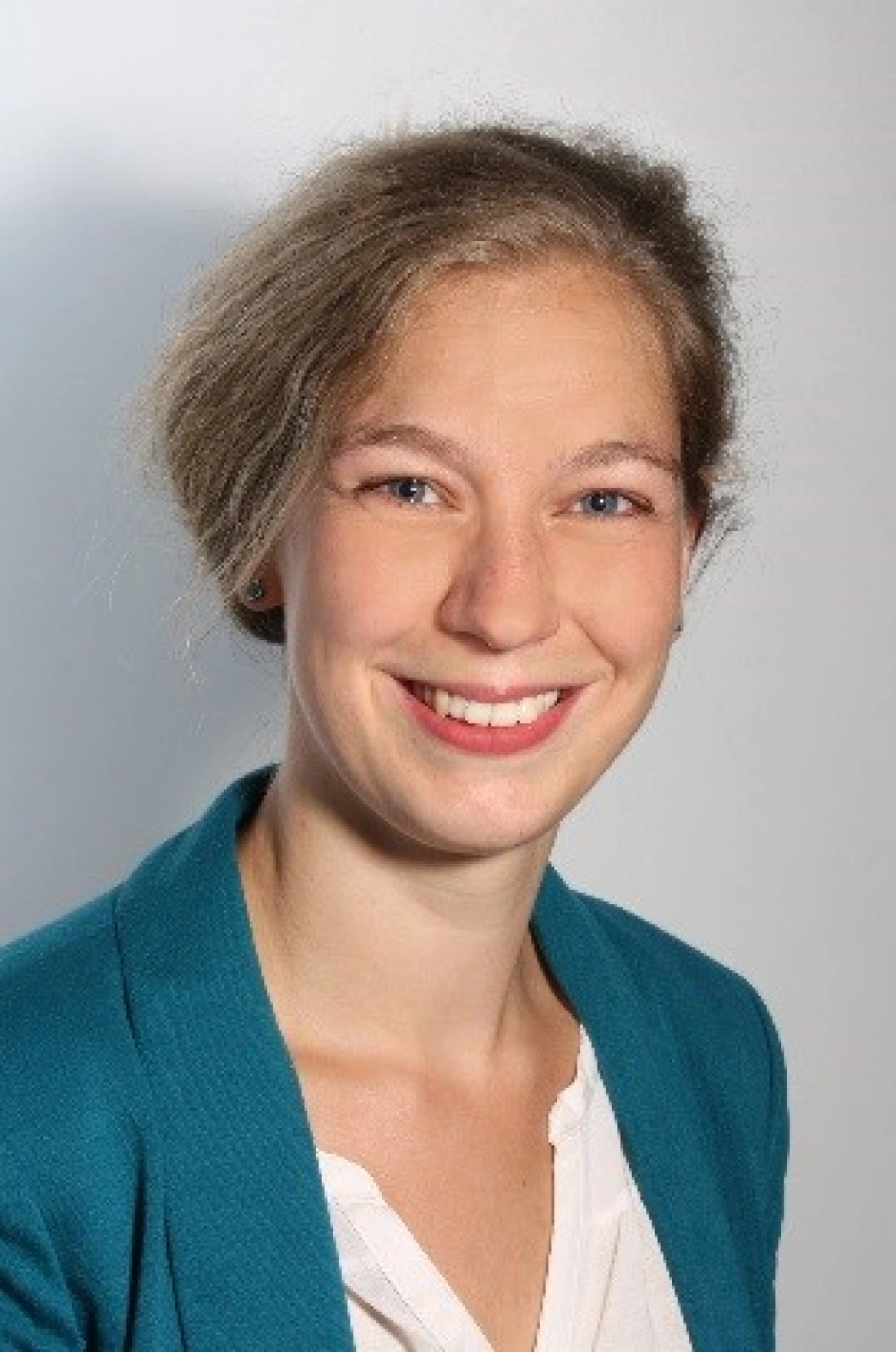 Młoda kobieta z uśmiechem, w niebieskim żakiecie, na jasnym tle.