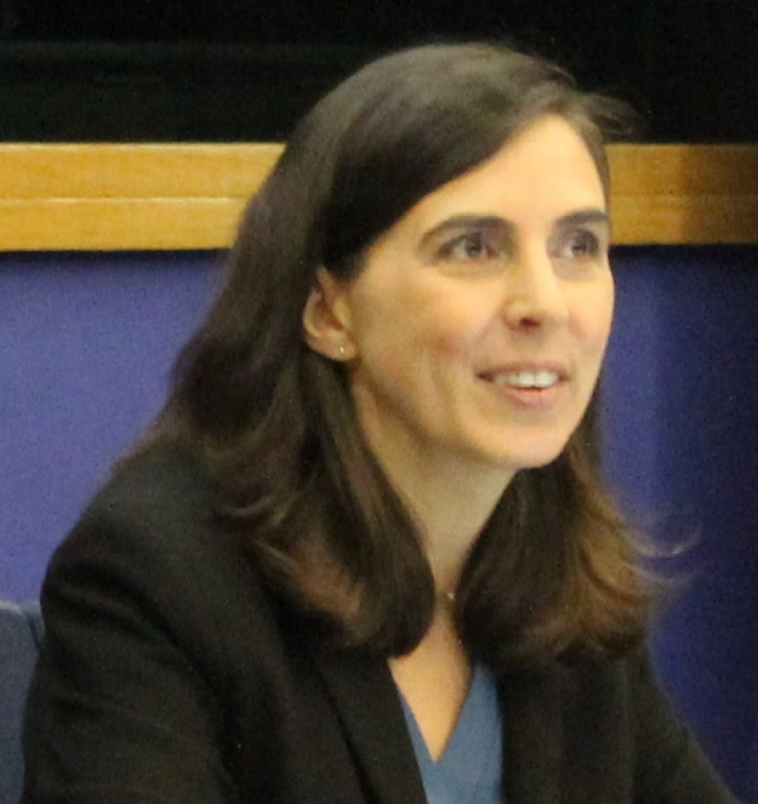 Uśmiechnięta kobieta z ciemnymi włosami, siedząca przy stole.