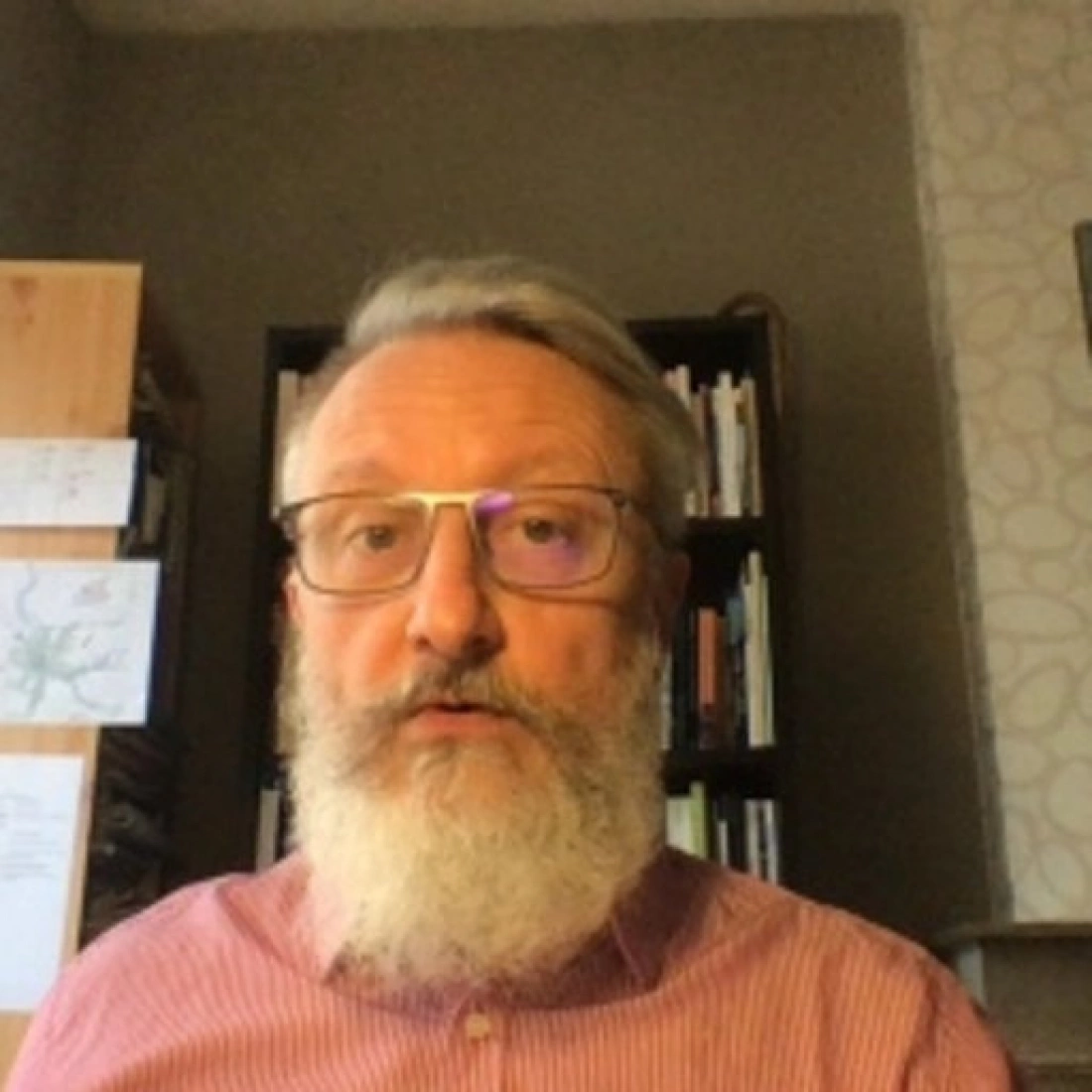 Mężczyzna z siwą brodą i okularami, siedzący w biurze z półkami książek w tle.