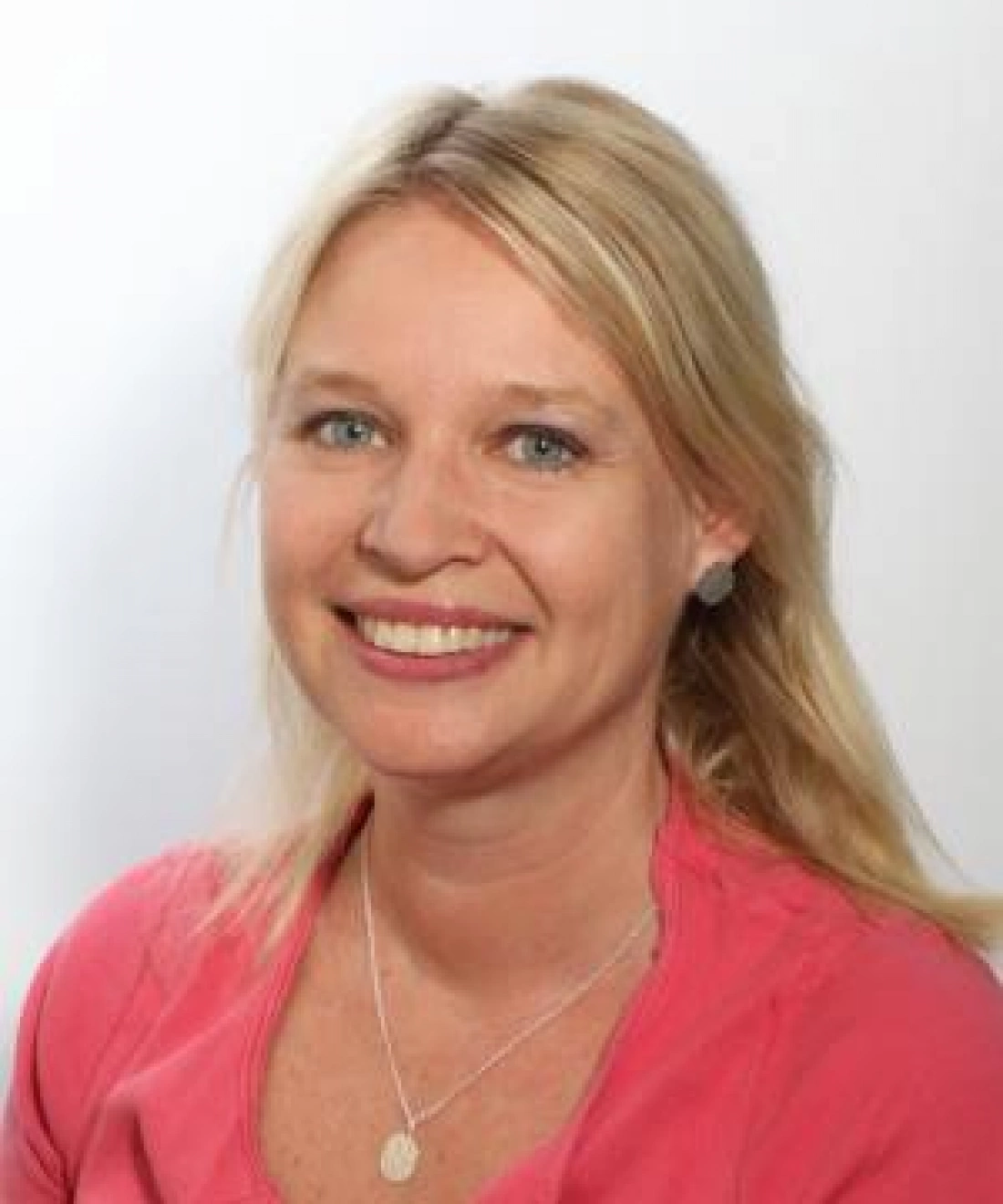 Kobieta z uśmiechem i blond włosami, ubrana w różową bluzkę.