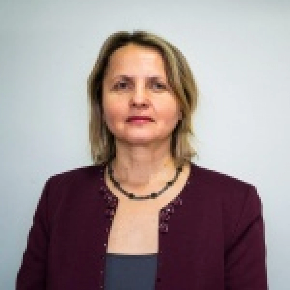 Kobieta w eleganckim stroju, stojąca na tle jasnej ściany.