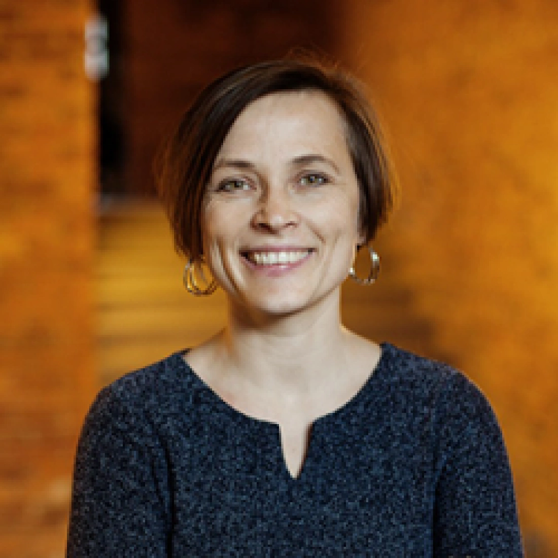 Uśmiechnięta kobieta w casualowym swetrze na tle ciepło oświetlonej przestrzeni.