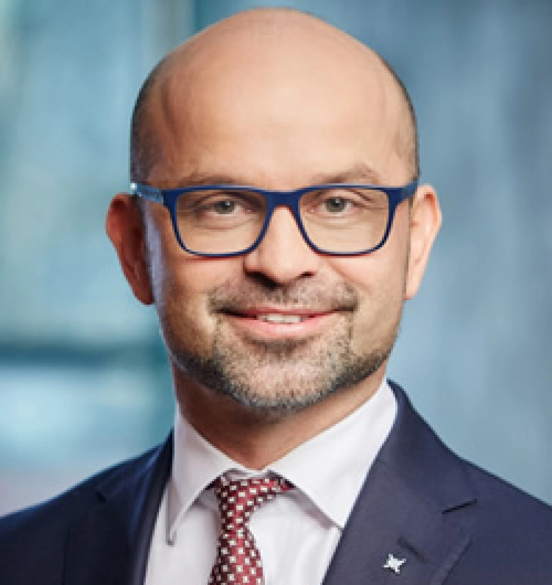 Mężczyzna w okularach, uśmiechający się w eleganckim garniturze.