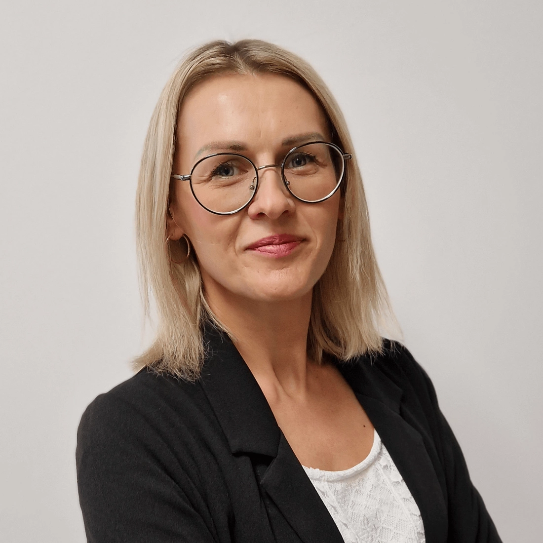 Kobieta w okularach, uśmiechająca się, ubrana w czarną marynarkę.