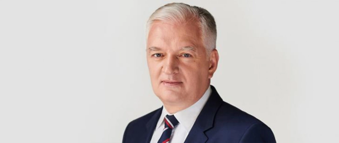 Mężczyzna w garniturze, z siwymi włosami, na neutralnym tle.