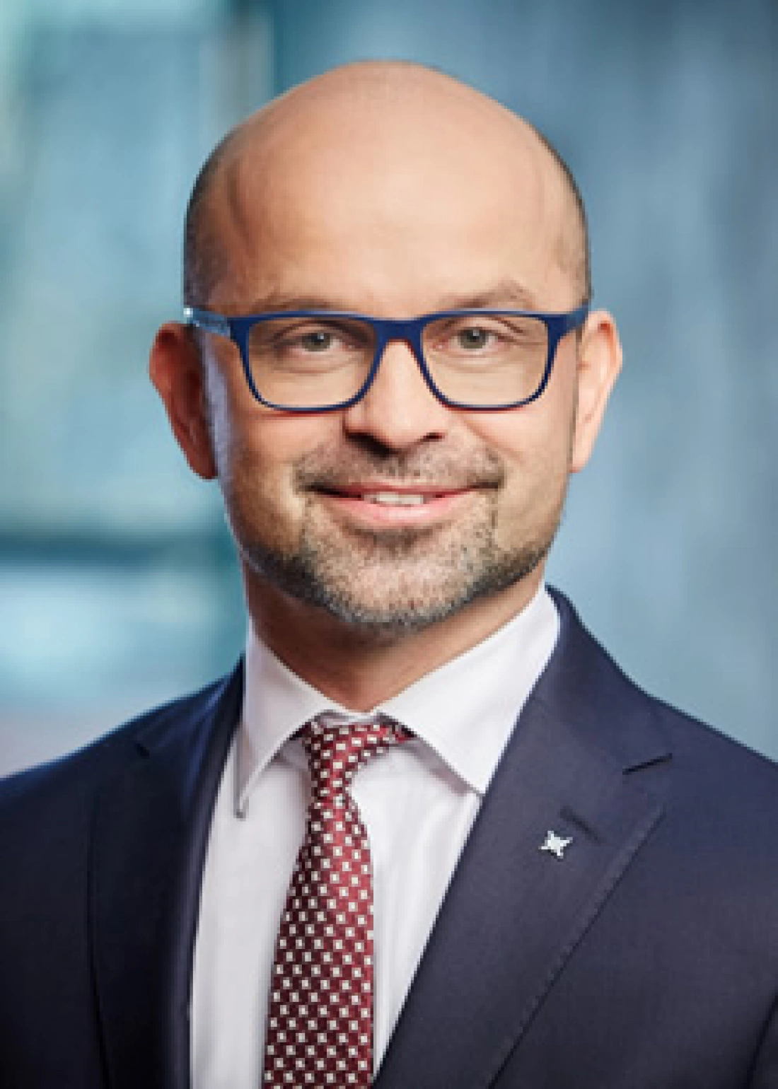 Mężczyzna w garniturze z okularami, uśmiechający się do kamery.