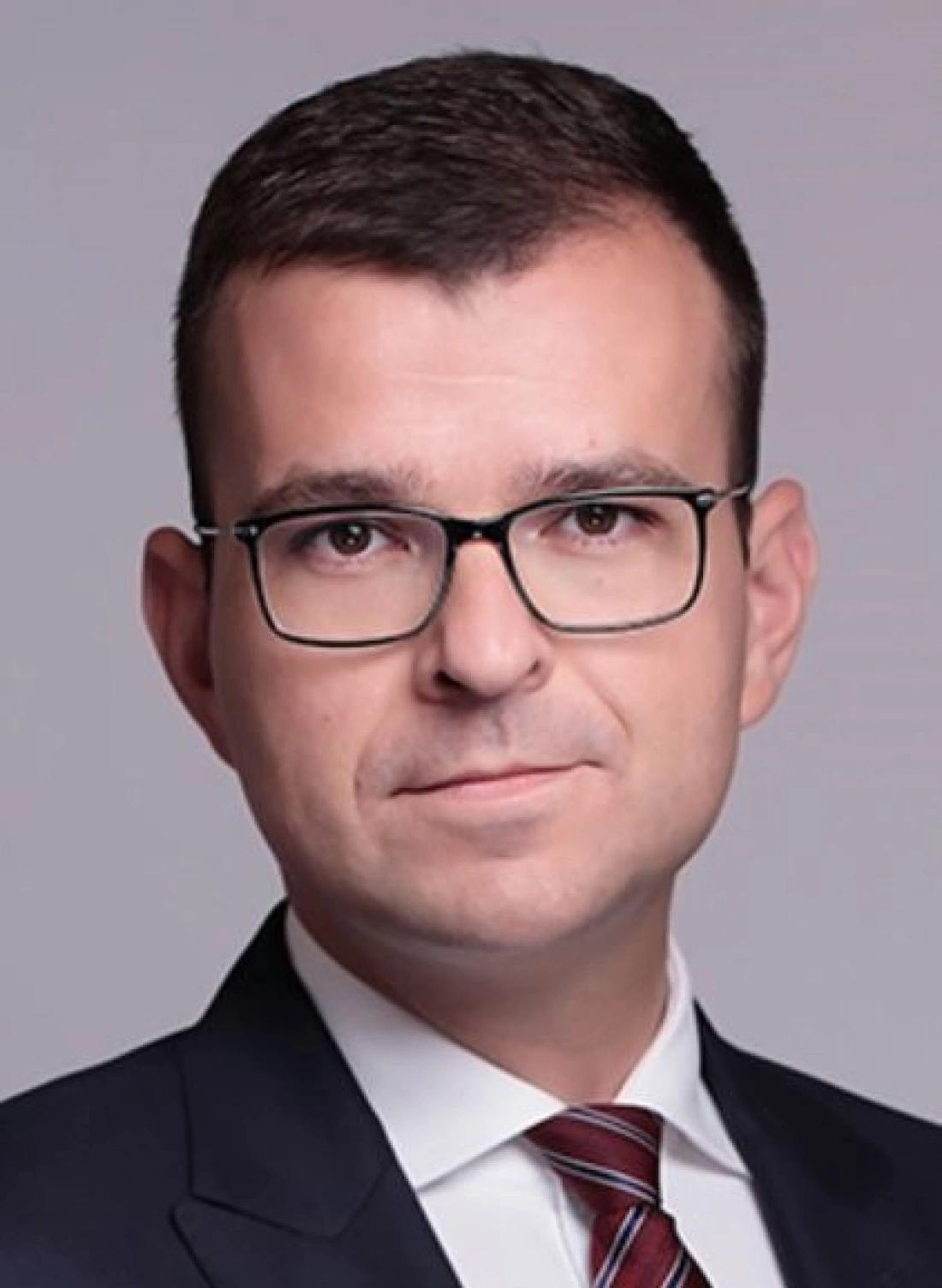 Mężczyzna w garniturze z okularami, prezentujący się poważnie.