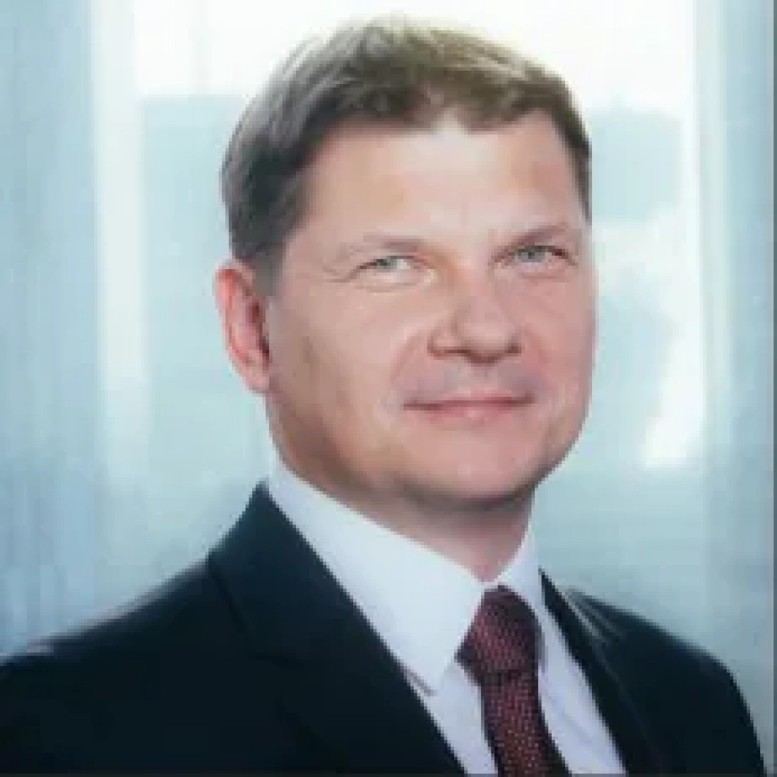 Mężczyzna w garniturze z uśmiechem na twarzy, w tle okno.