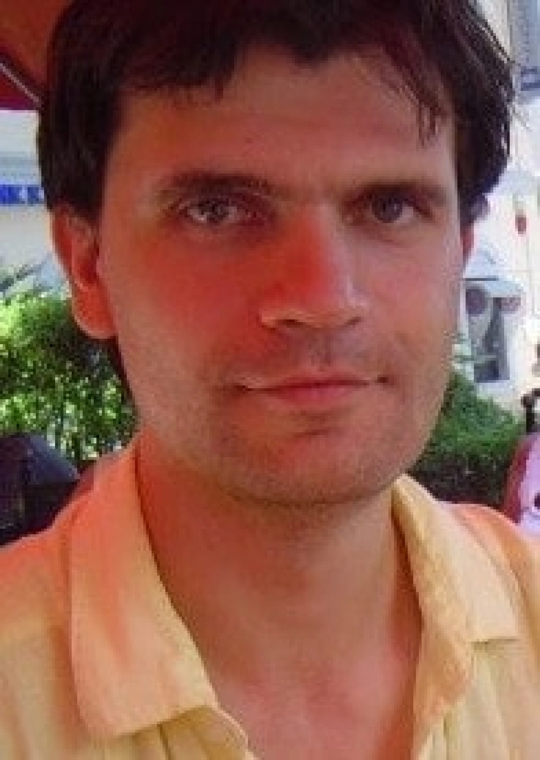 Portret mężczyzny w jasnej koszuli, z lekko zarośniętą twarzą i naturalnym wyrazem. Tło w delikatnych kolorach.