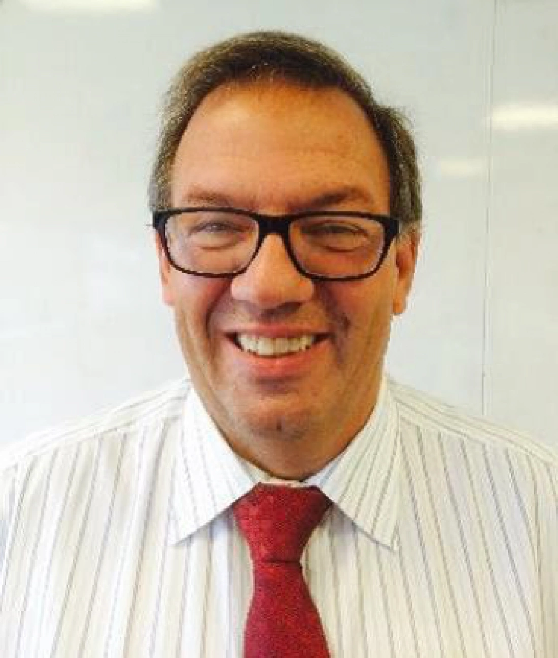 Mężczyzna w okularach, uśmiechający się, ubrany w biały, prążkowany koszulę i czerwoną krawatę.