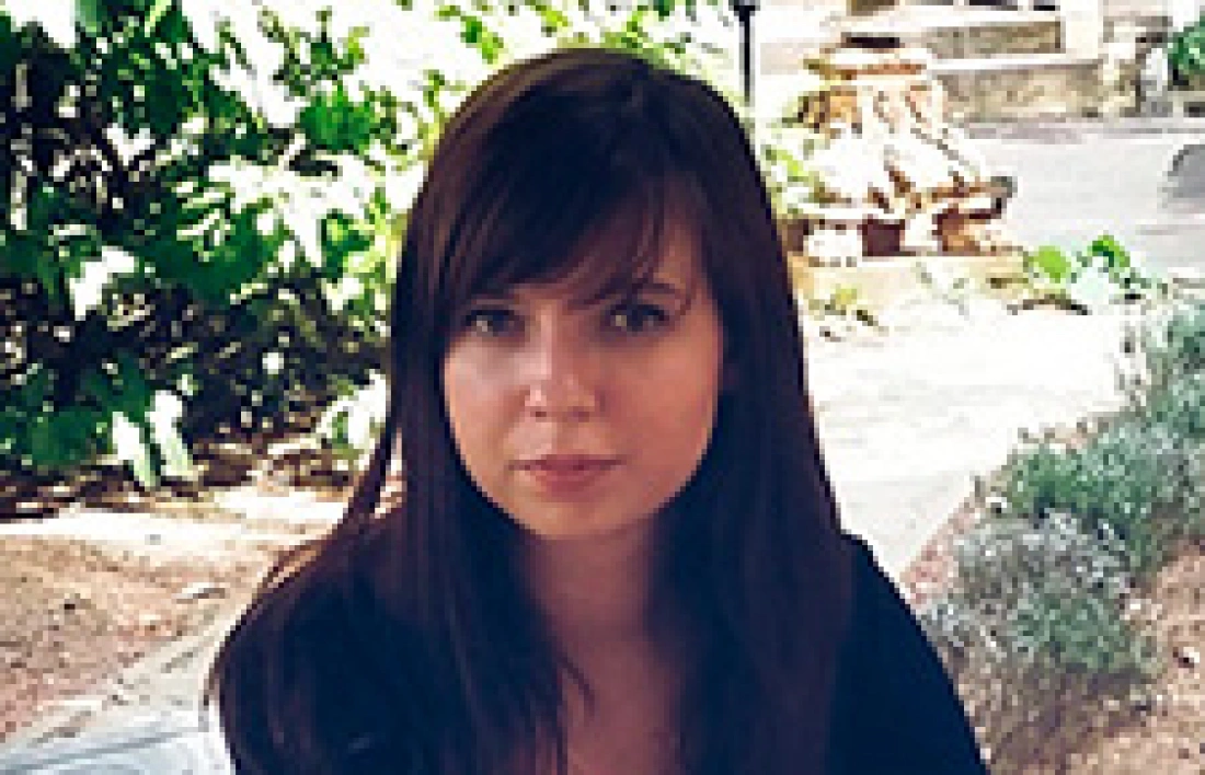 Kobieta o długich włosach siedząca na zewnątrz w otoczeniu zieleni.