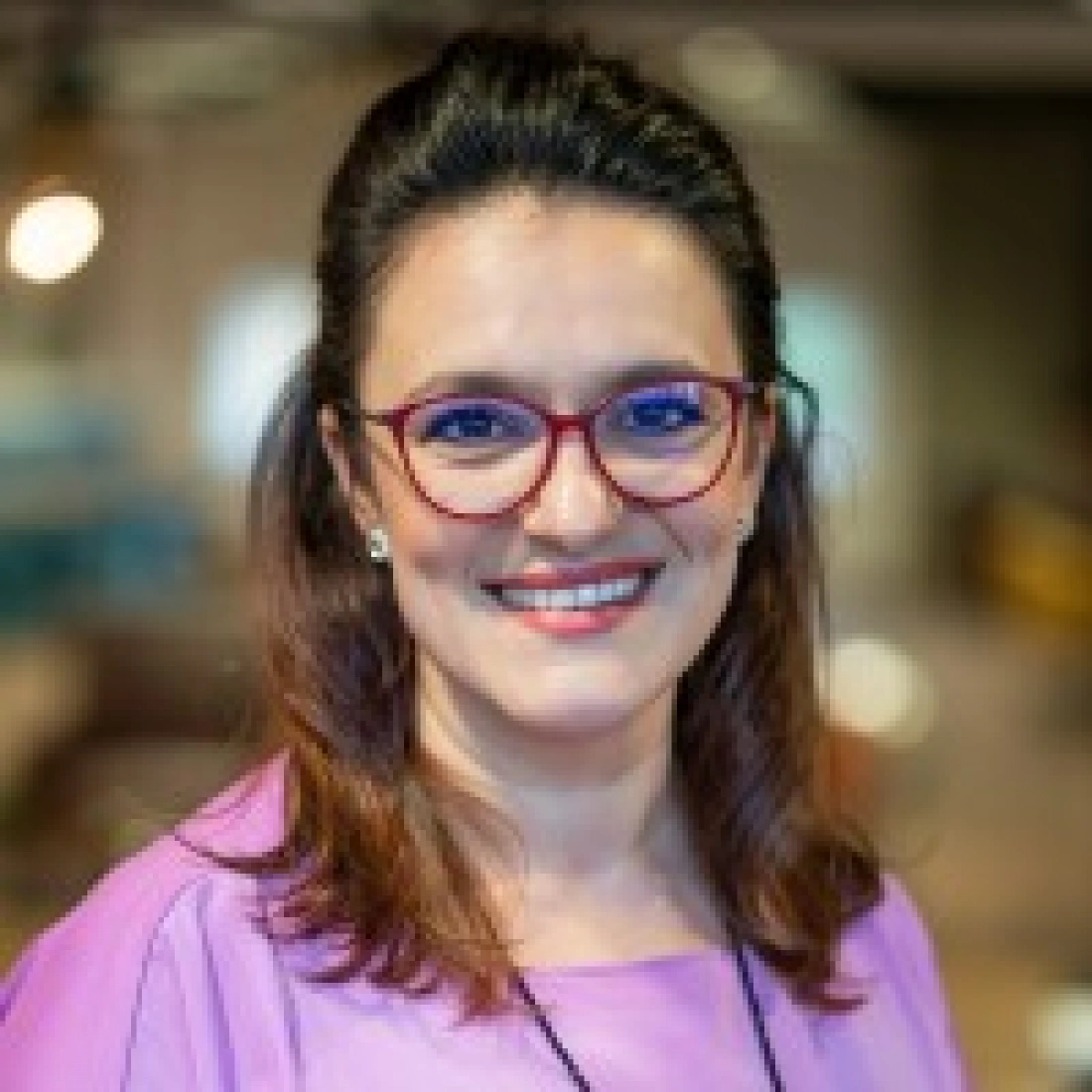 Kobieta w różowej bluzce z okularami, uśmiechająca się.