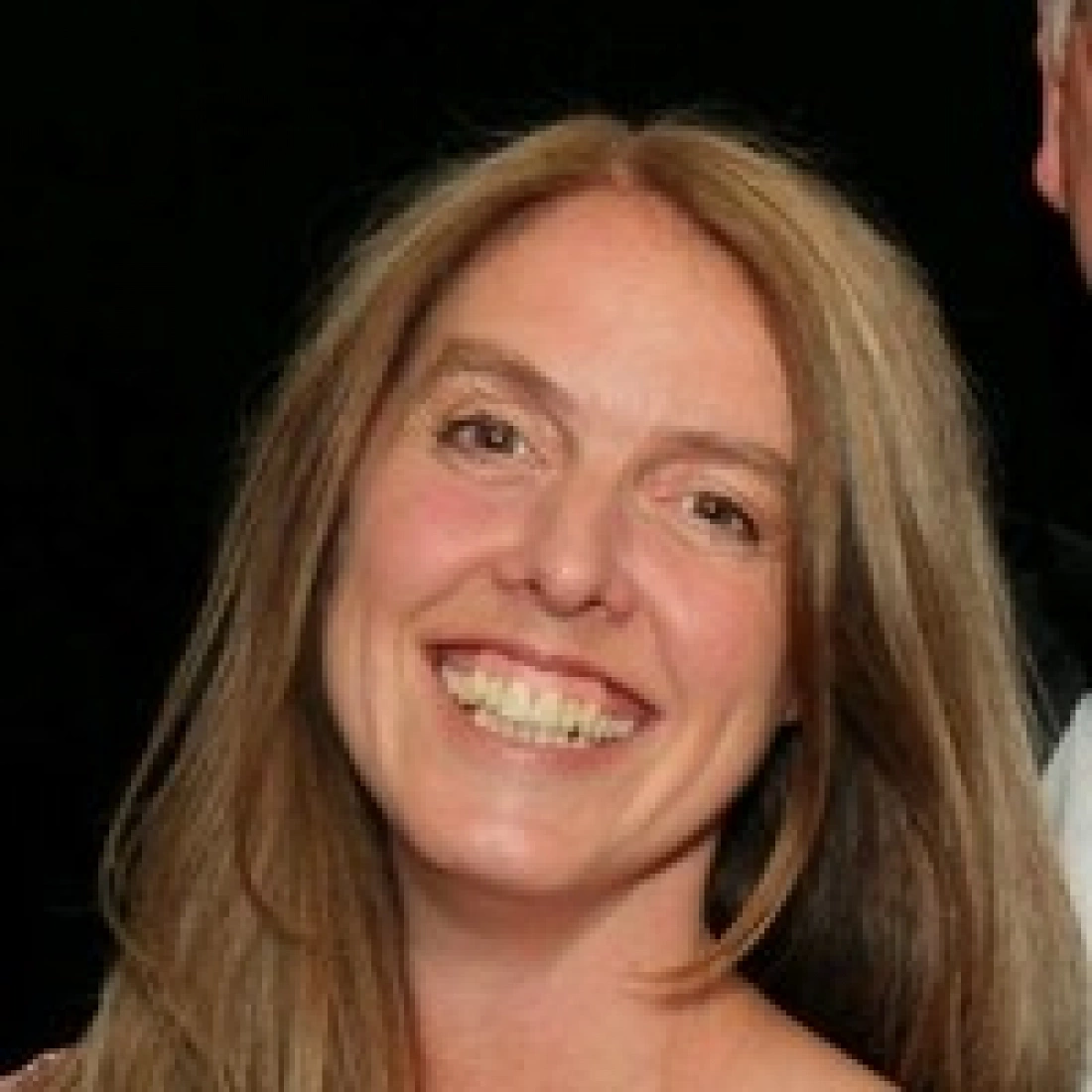 Uśmiechnięta osoba z długimi włosami na ciemnym tle.