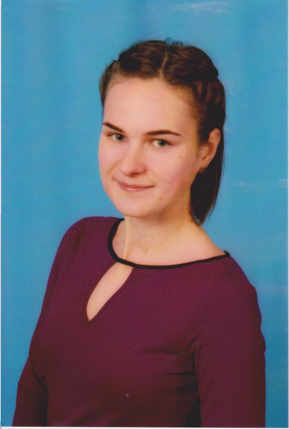 Młoda kobieta z uśmiechem, ubrana w fioletową bluzkę, na tle niebieskiej ściany.