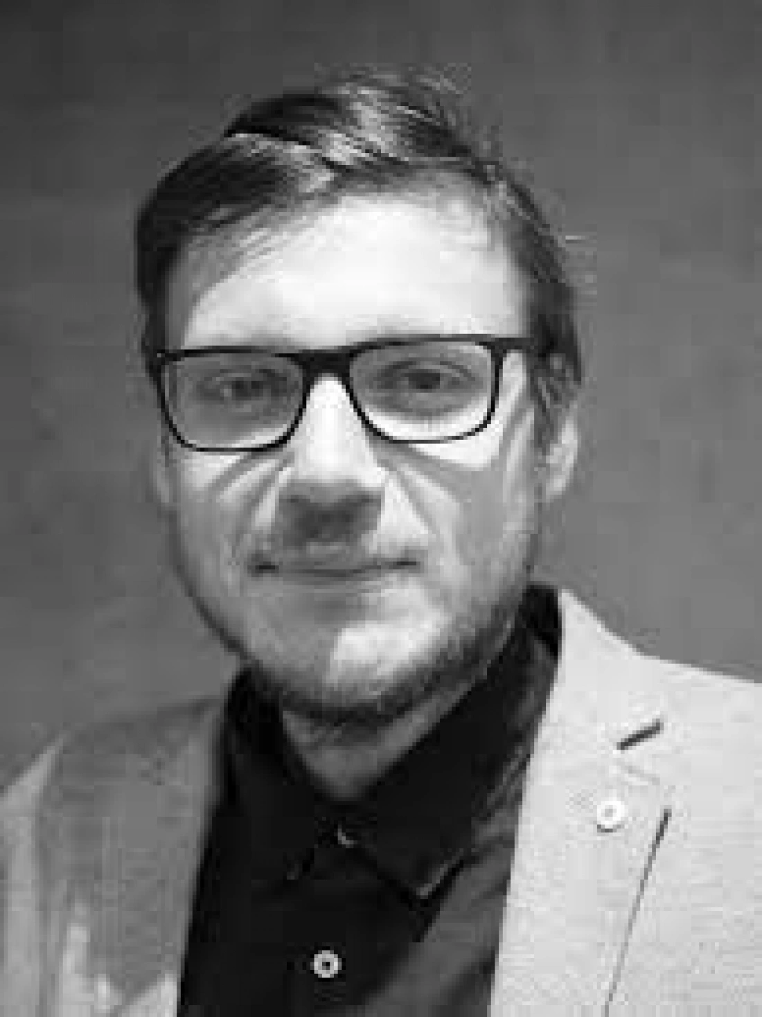 Mężczyzna w okularach, w szarym żakiecie, uśmiechający się do kamery.