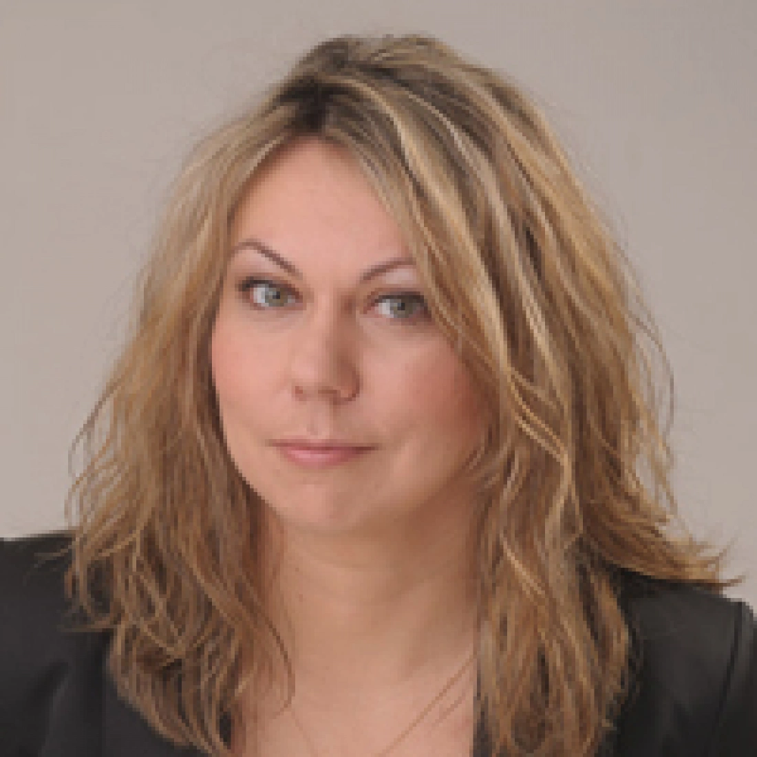 Kobieta z długimi, falującymi włosami, uśmiechająca się lekko, w czarnym żakiecie.