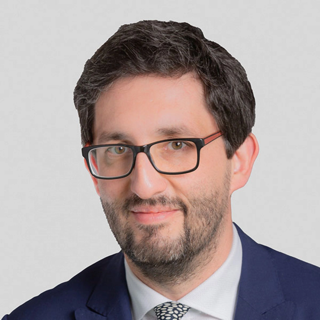 Mężczyzna w okularach, uśmiechający się, w garniturze na jasnym tle.