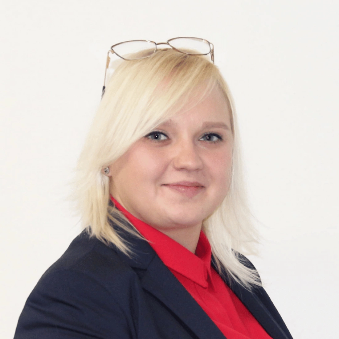 Kobieta z blond włosami w garniturze, uśmiechająca się, z okularami na głowie.