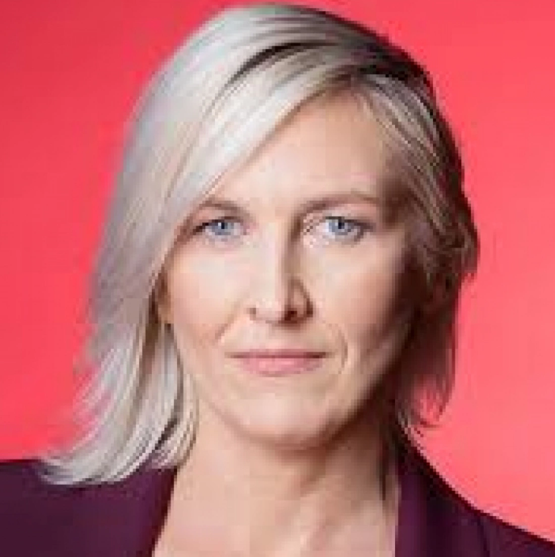 Kobieta z jasnymi włosami i niebieskimi oczami na tle różowym.