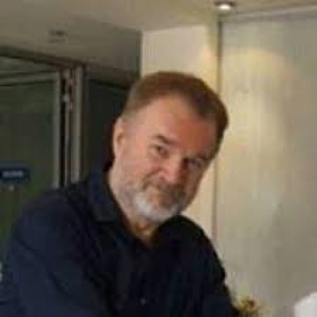 Mężczyzna z brodą, uśmiechający się w pomieszczeniu.