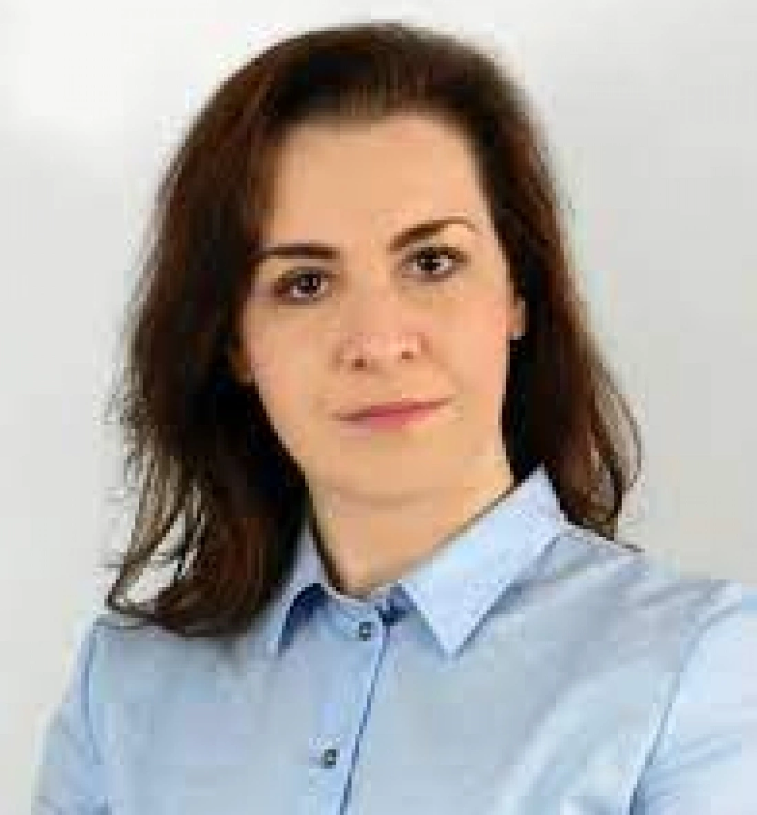 Kobieta o brązowych włosach w niebieskiej koszuli, pozująca na jasnym tle.