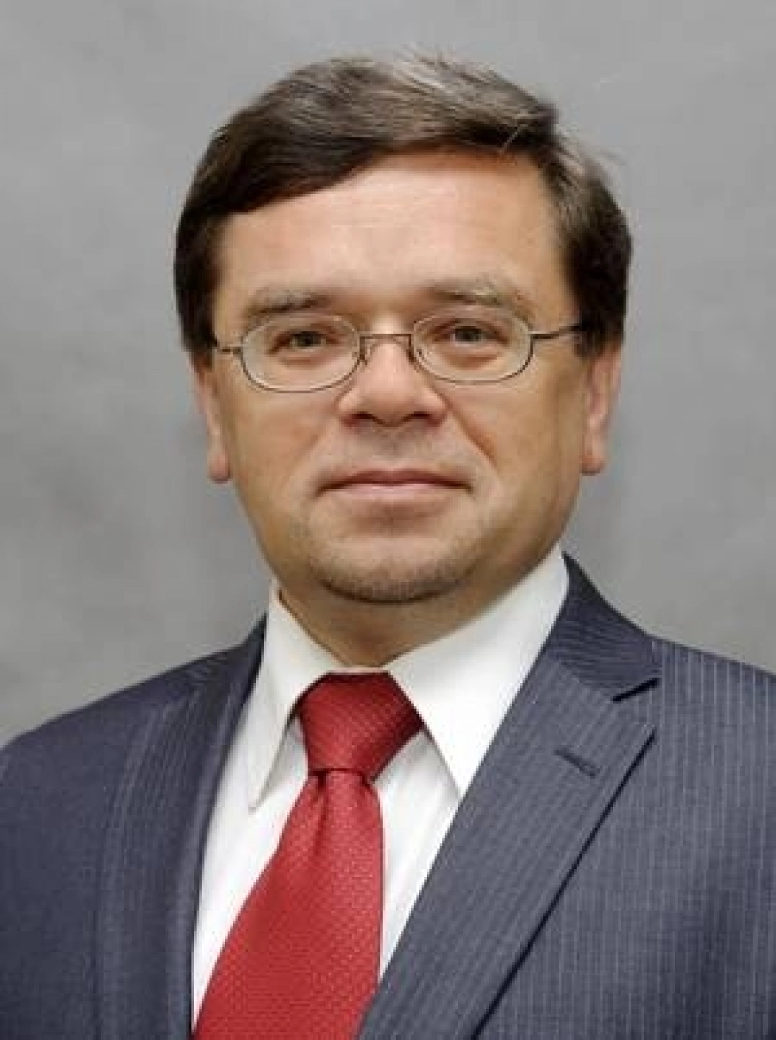 Mężczyzna w eleganckim garniturze z czerwonym krawatem, uśmiechający się do kamery.