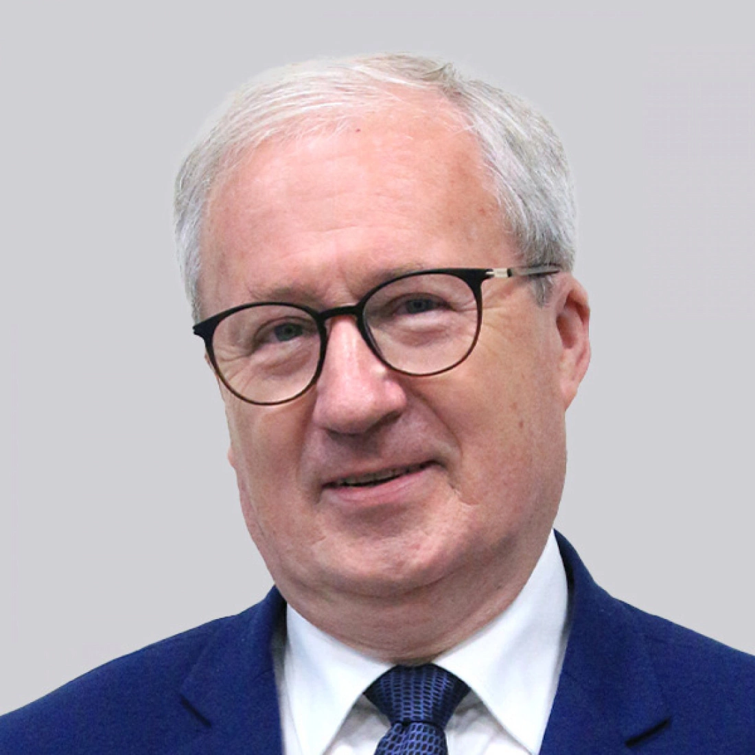 Mężczyzna w okularach, uśmiechający się w niebieskim garniturze.