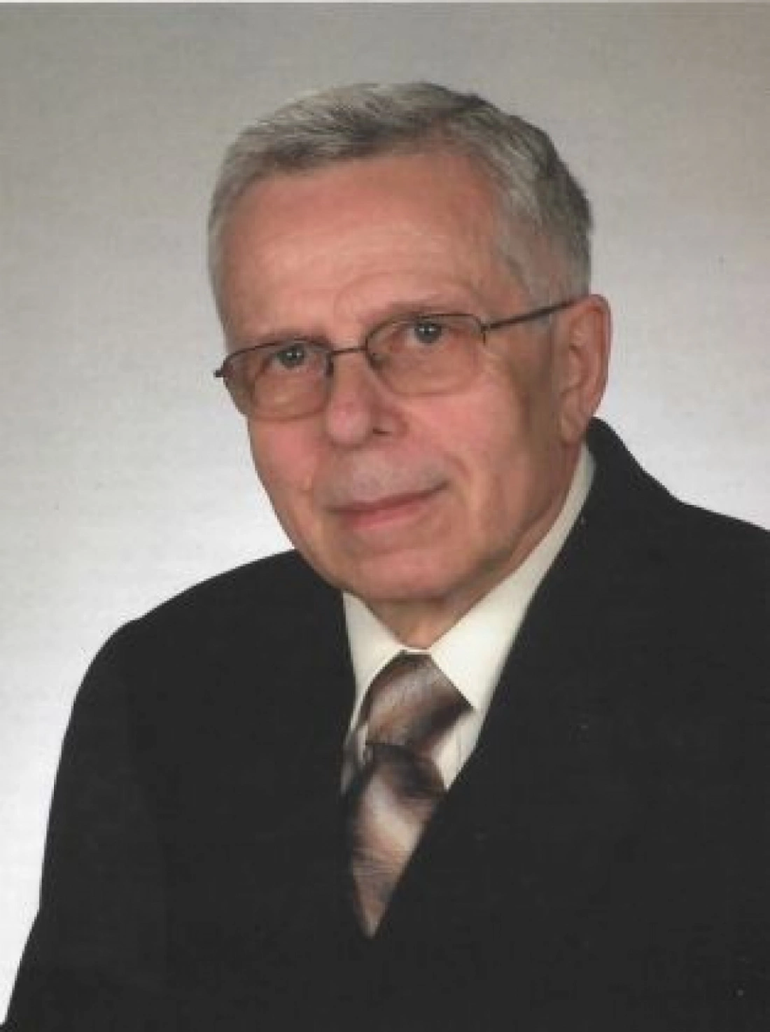 Starszy mężczyzna w okularach, w eleganckim garniturze i krawacie.