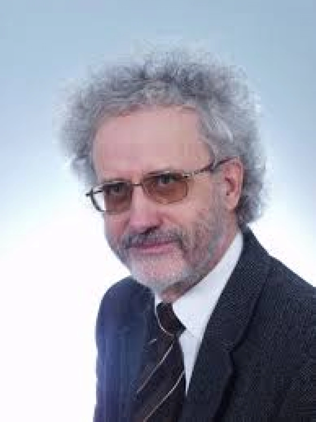 Mężczyzna w okularach z siwymi włosami i zarostem, ubrany w elegancki garnitur.