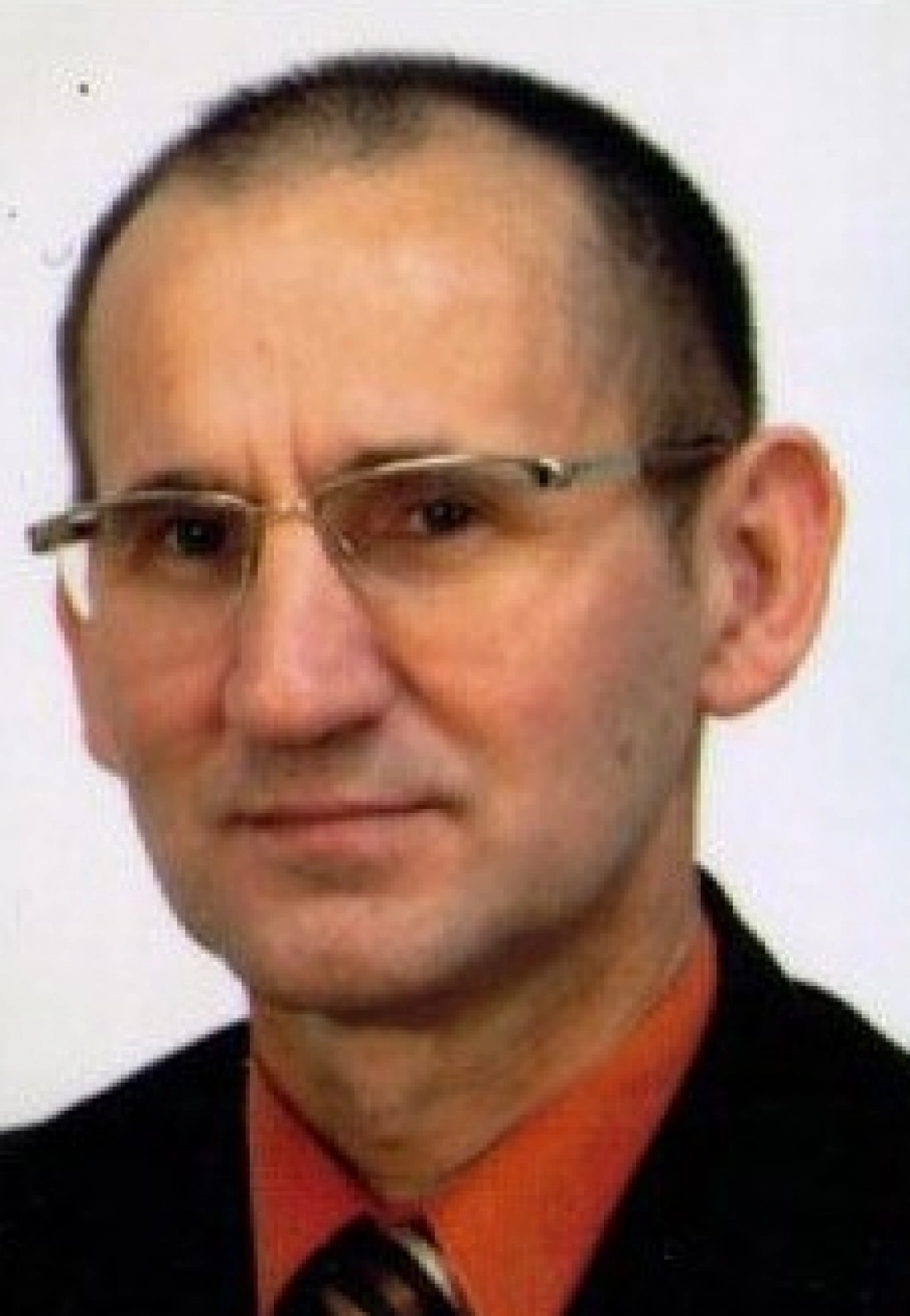 Mężczyzna w okularach, uśmiechający się, w eleganckim garniturze.