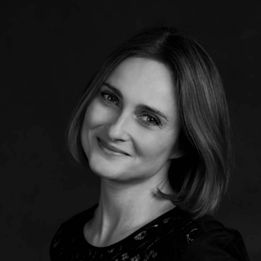 Portret policjantki w mundurze, z uśmiechem na twarzy. W tle kolejny funkcjonariusz.